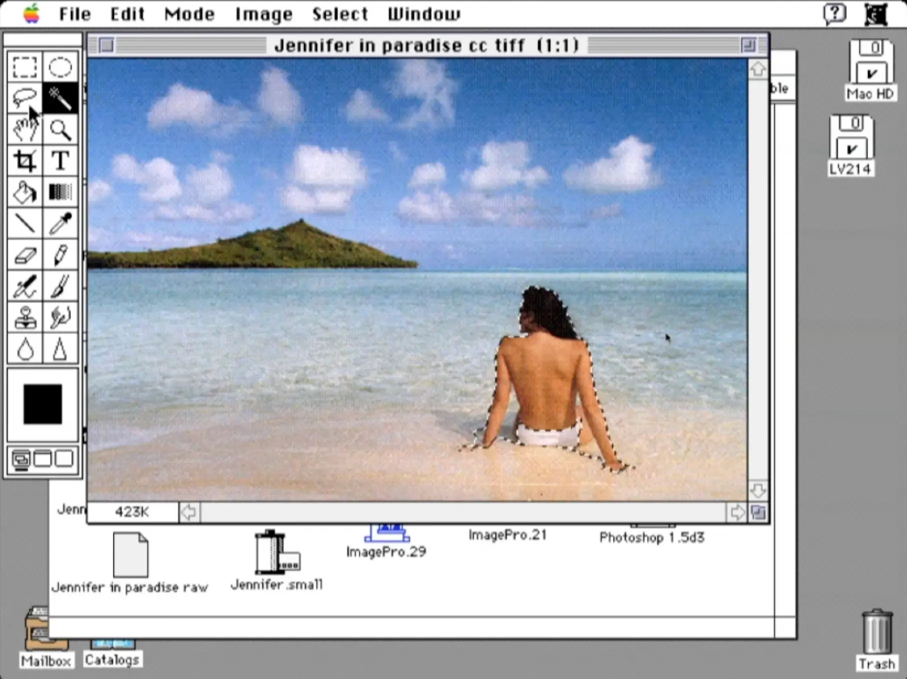 On a screenshot of a computer desktop running an early version of Photoshop software, a topless white woman, seen from behind, sits at the edge of a clear sea on a picturesque beach, gazing at an island on the horizon under a bright blue sky